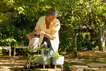 Watering plants in garden, mature woman enjoying gardening in backyard