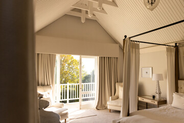 Bright bedroom with canopy bed and cozy seating area near large window, copy space