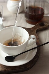 Pouring hot water into cup with tea bag on light table, closeup