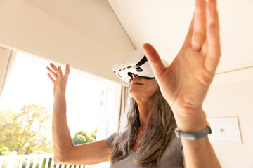 Using VR headset, mature woman exploring virtual reality at home