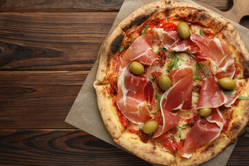 Tasty pizza with cured ham, olives and sun-dried tomato on wooden table, top view. Space for text
