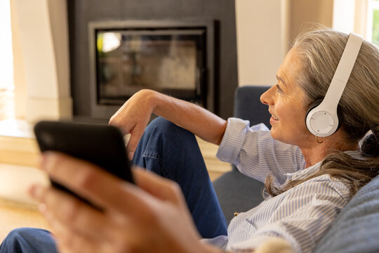 Listening to music with headphones, mature woman relaxing and holding smartphone