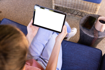 Naklejka premium Using tablet while sitting on couch, young woman relaxing at home, copy space