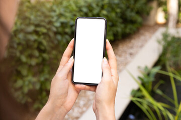 Holding smartphone with blank screen, person outdoors in garden setting, copy space