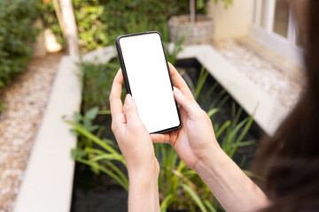 Holding smartphone with blank screen, person standing near garden pond, copy space