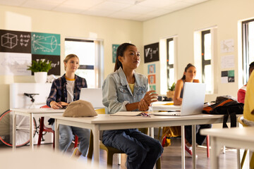 In high school, teenagers using laptops and listening attentively in classroom