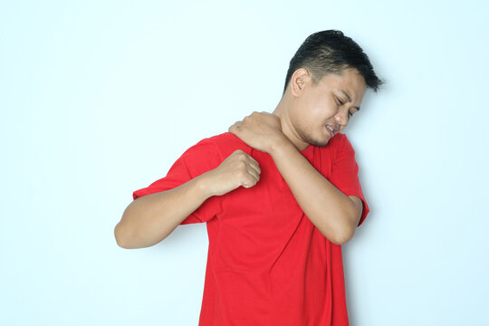 Young Asian man touching his right shoulder with pain expression. Wearing red t-shirt