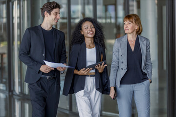 Diverse group businesspeople walking to meeting at modern office. Businessmen and businesswoman chatting talk with tablet and document paper. Manager orders work on way to office.