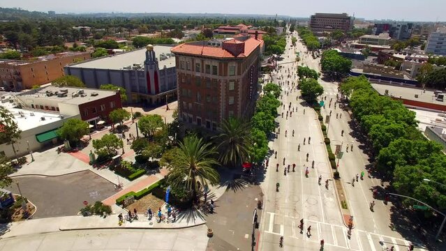 Aerial Panning Crowd Of People Cycling By The Culver Hotel In Residential City On Sunny Day - Los Angeles, California