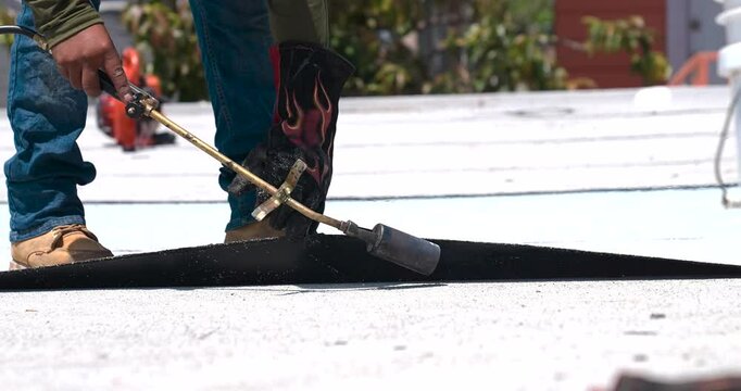 Roofer applying granulated APP Torch Down and Using a Roller