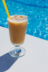 alcohol spirits drink beverage cocktail Irish cream liqueur pouring into a glass full of ice near the swimming pool with blue water. Summer vacation or party. Vertical