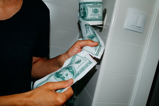cutting a piece of toilet paper patterned with 100 dollar bills
