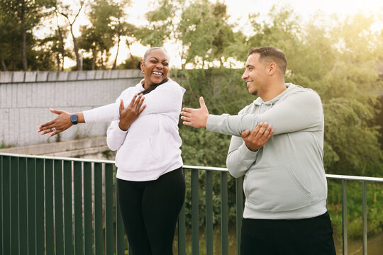 Joyful Dominican couple with curvy body types warming up arms