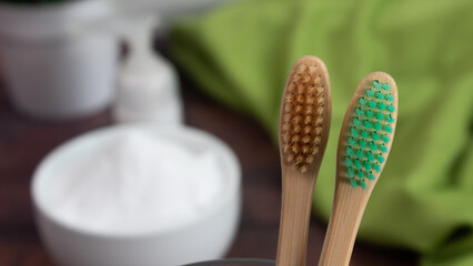 Pair of bamboo toothbrushes in glass cup on wooden table, organic toothpaste in the background. Sustainable dental hygiene