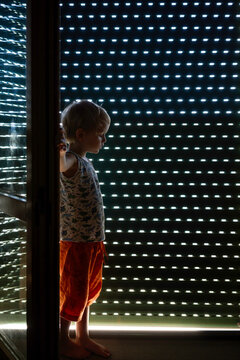 Child standing  in darkened room by terrace door shutter