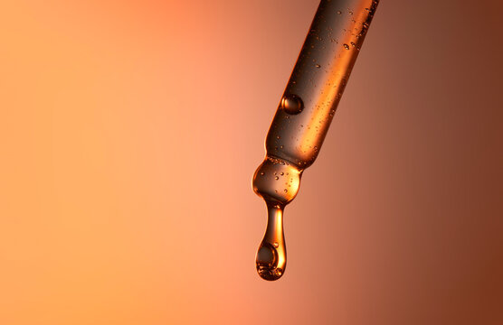Clear glass pipette with a drop of cosmetic product falling down. 