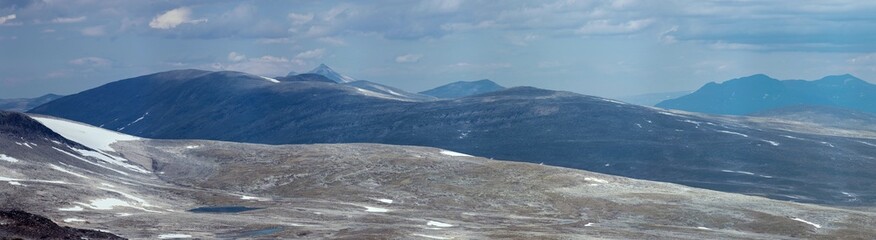 Wild barren mountain tops in a vast empty polar landscape of northern Norway. In the distance a pointy peak, as a view from Bolnatind, Helgeland, Norway. Fjell of the arctic circle. Cold blue mountain
