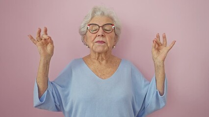 Beautiful middle-aged woman in glasses, grey-haired and radiant, meditates with ease and grace. she stands over a pink backdrop, eyes closed in a yoga pose, embodying wellness and serenity - Powered by Adobe