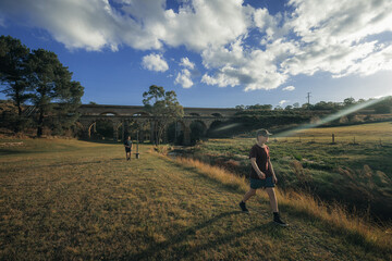 Teenage boys walking through paddock with historic bridge in background
