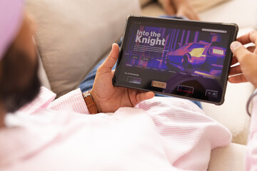 Holding tablet, man browsing video streaming service while relaxing at home