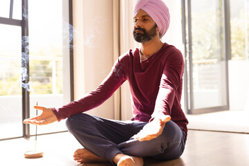 Meditating at home, Indian man sitting cross-legged with incense burning