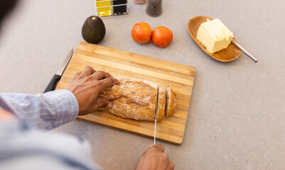 Cutting bread on wooden board, man preparing ingredients with avocado and tomatoes