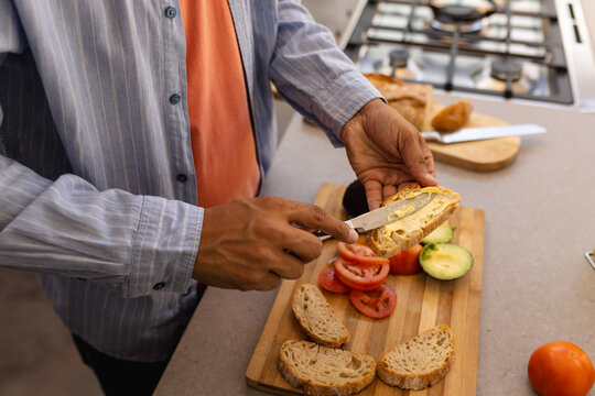 Spreading butter on bread, man preparing sandwich with fresh vegetables in kitchen - Powered by Adobe