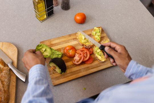 Preparing avocado and tomato toast, man slicing vegetables on wooden cutting board