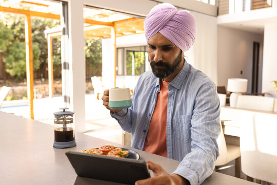 Drinking coffee and using tablet, man enjoying breakfast at home