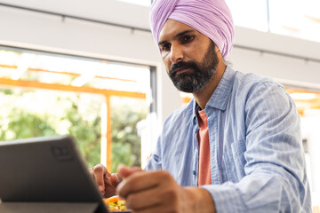 Working from home, man using tablet and eating meal at table