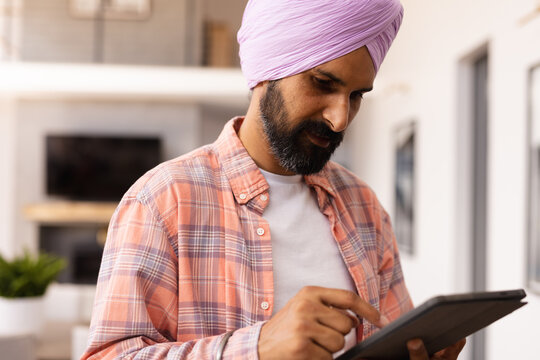 Using tablet, man in turban focusing on work at home - Powered by Adobe