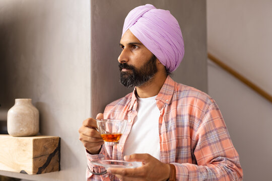 Holding cup of tea, man in turban standing and looking away - Powered by Adobe