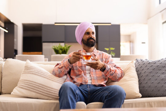 Relaxing on sofa, Indian man enjoying cup of tea at home