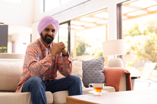 Sitting on sofa, man with turban relaxing at home with cup of tea, copy space - Powered by Adobe