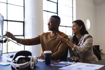 Collaborating in office, colleagues pointing at computer screen discussing project