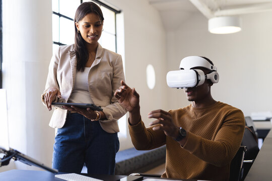 Using VR headset, man interacting while woman holding tablet in office