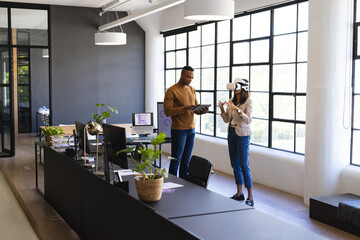 Using VR headset, businesswoman discussing project with colleague in modern office