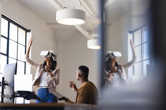 Using VR headset in office, woman exploring virtual environment while colleague observes