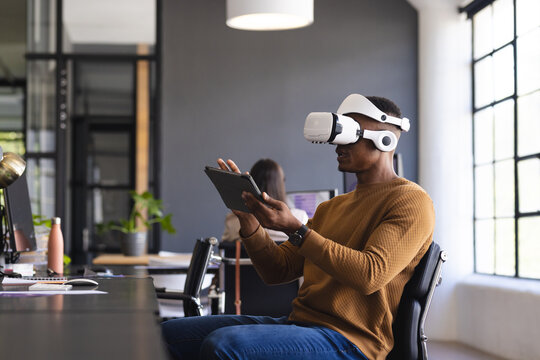 Using VR headset, man interacting with tablet in modern office workspace