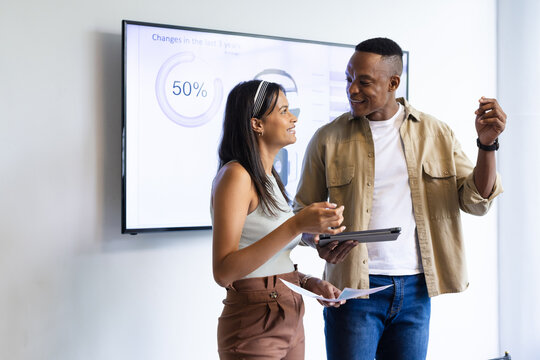 Presenting business data, colleagues using tablet and charts discussing statistics in office