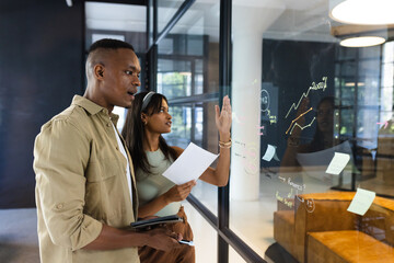 Discussing business strategy, colleagues analyzing charts and graphs on glass wall