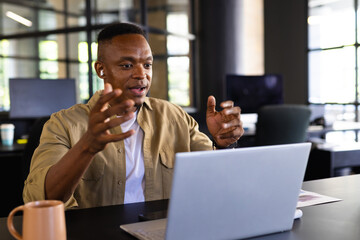 Businessman using laptop, gesturing during video conference call in modern office