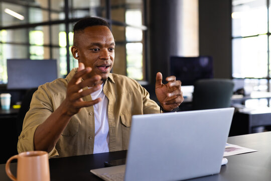 Businessman using laptop, gesturing during video conference call in modern office