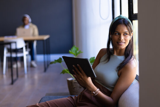 Holding tablet, woman smiling and looking out window in modern office, copy space