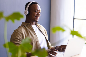 Using laptop and wearing headphones, man smiling while working from home office