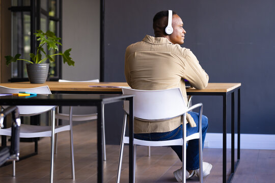 Listening to music, man wearing headphones sitting at desk in modern office, copy space