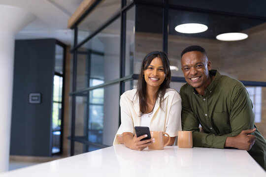 Smiling business colleagues with coffee cups, using smartphone in modern office, copy space