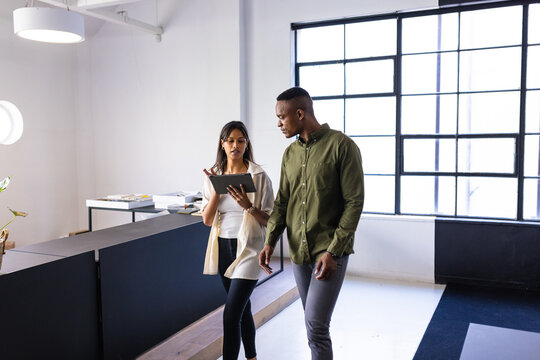Discussing work, colleagues walking in modern office while using digital tablet