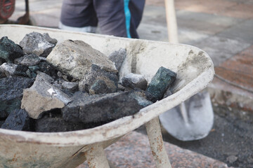 Wheelbarrow with materials on worksite, worker unloading rocks and gravel onto pavement