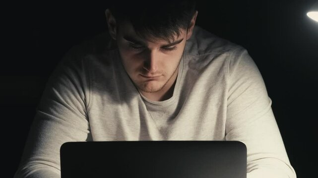 Deadline burnout. Work frustration. Job challenge. Sleepy prostrated male freelancer typing on laptop at desk yawning late in dark room.